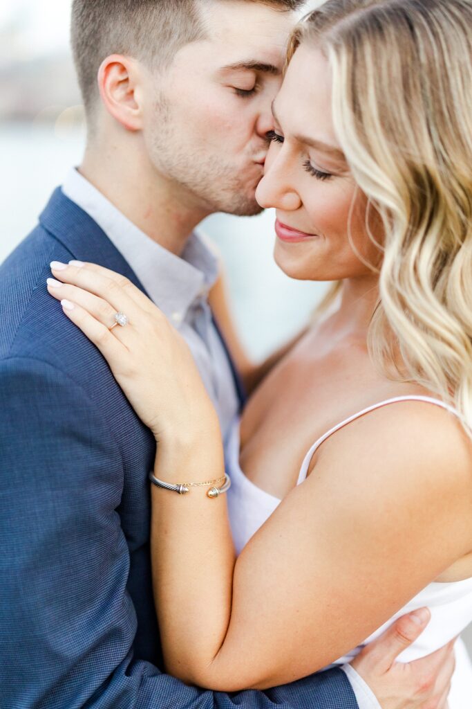 groom kissing brides cheek while she smiles at her ring on his shoulder