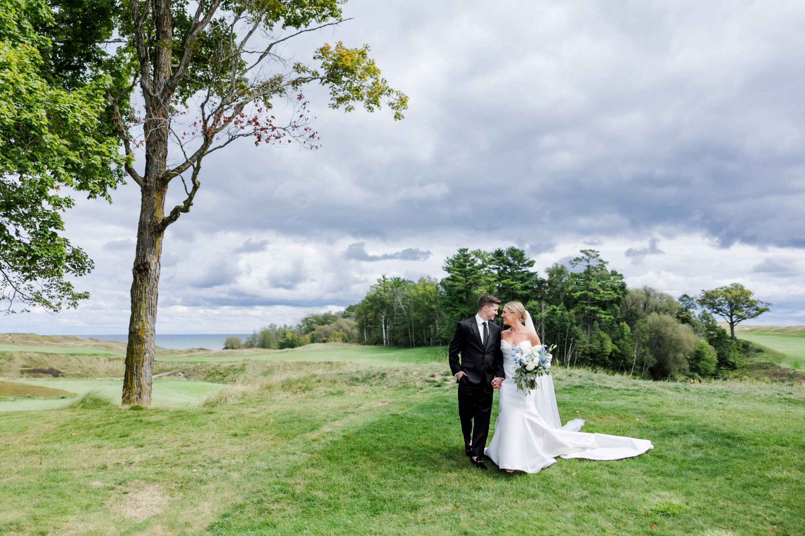 bride and groom walking closely with stormy clouds near a golf course.
